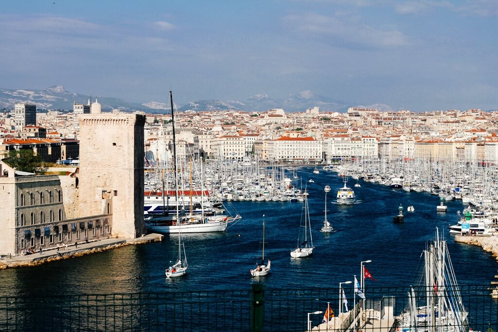 The harbour in Marseille from above with yachts and pale buildings with red roofs.