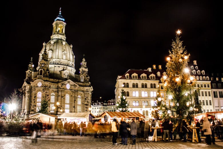 Dresden Christmas Market at Neumarkt at night with people standing around in groups.